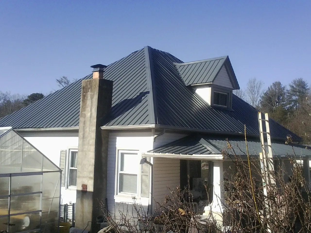 Dark blue standing seam metal roof on a white farmhouse with dormer — Slate & Tile Roof Repair by Roofing Brothers in West New York