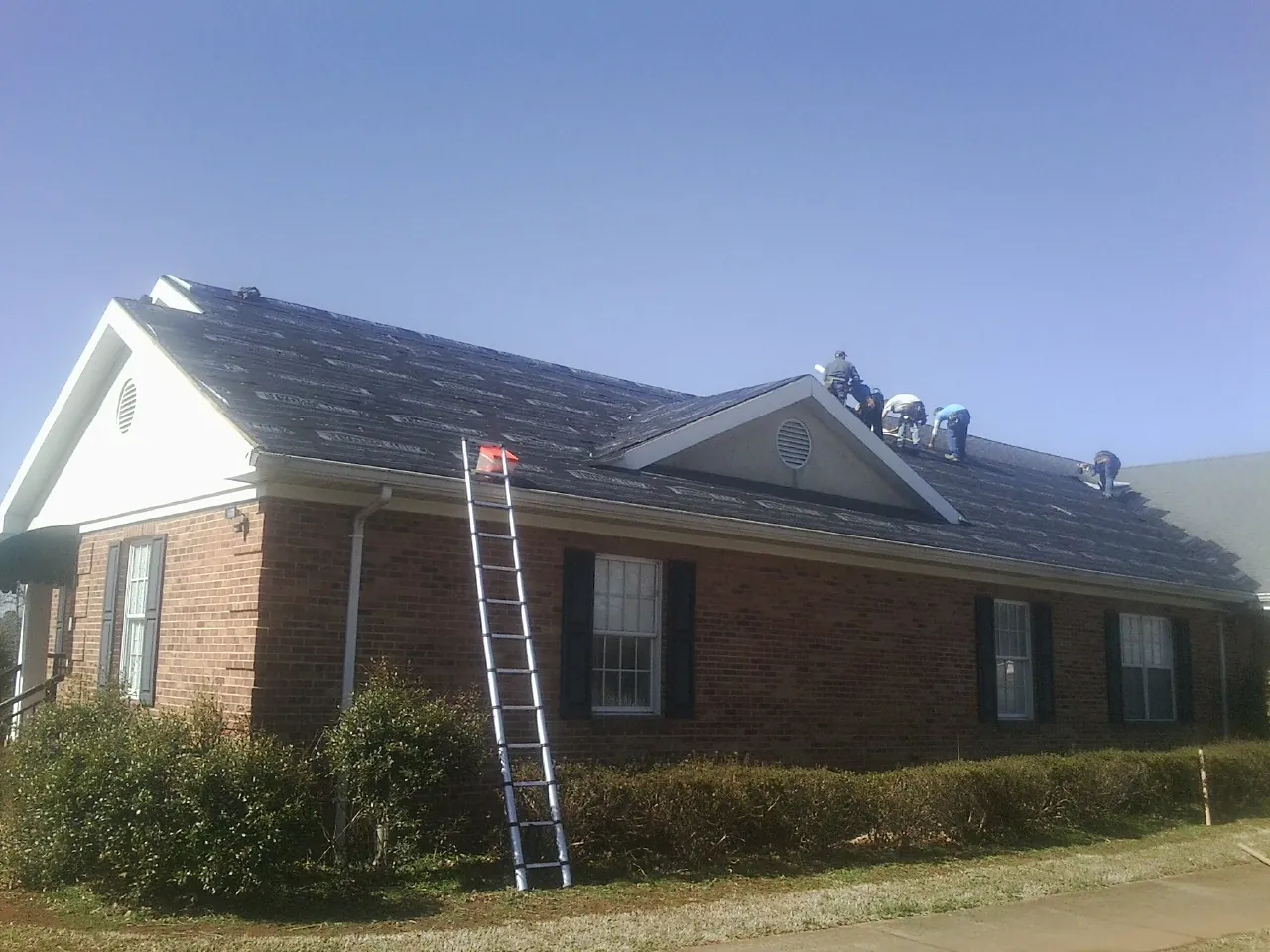 Crew tearing shingles off a brick ranch roof with a ladder set — Emergency Roof Repair work by our crew in West New York