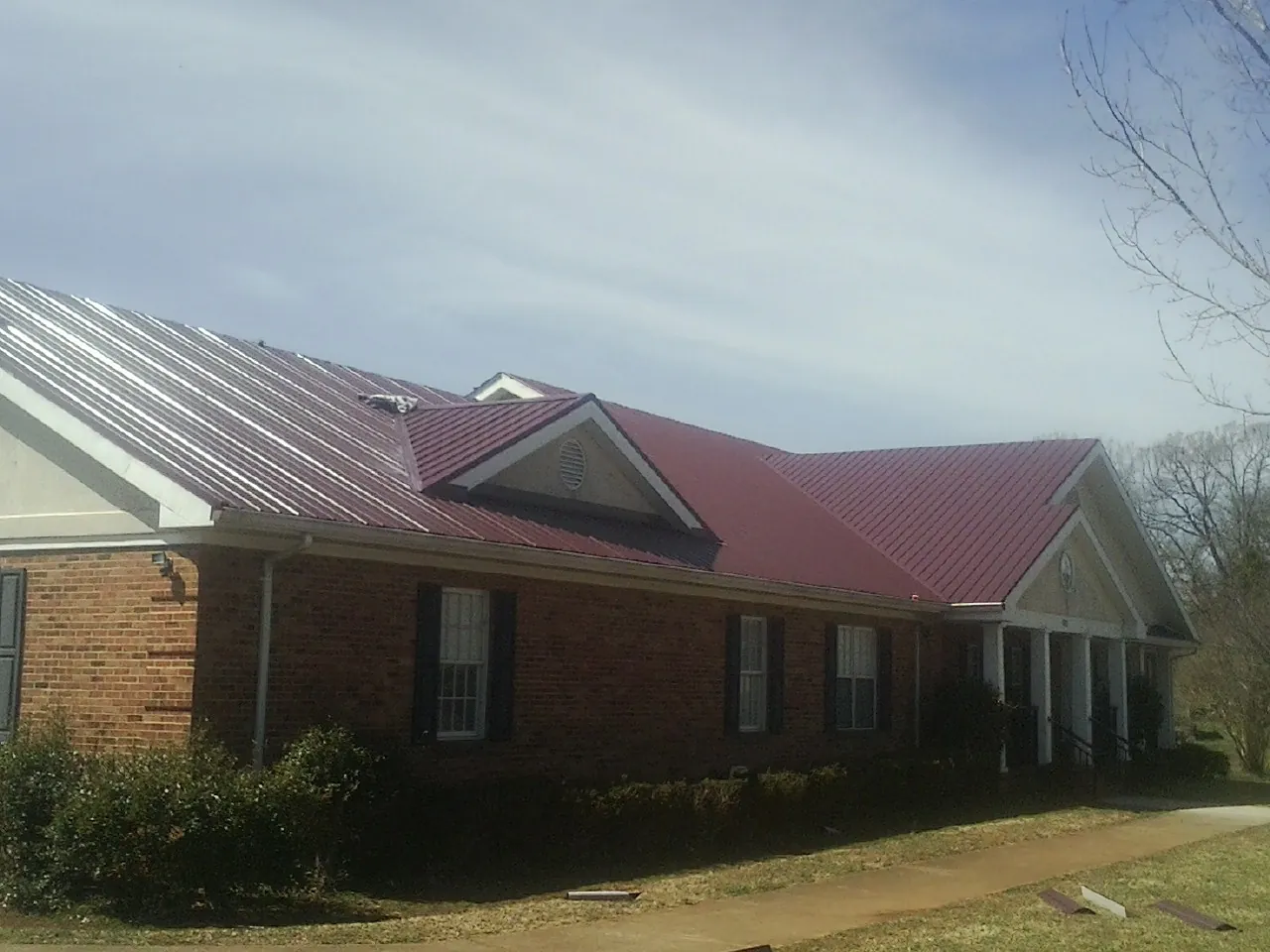 Red metal roof with gabled entries on a long brick building, from a Hail Damage Roof Repair job in West New York