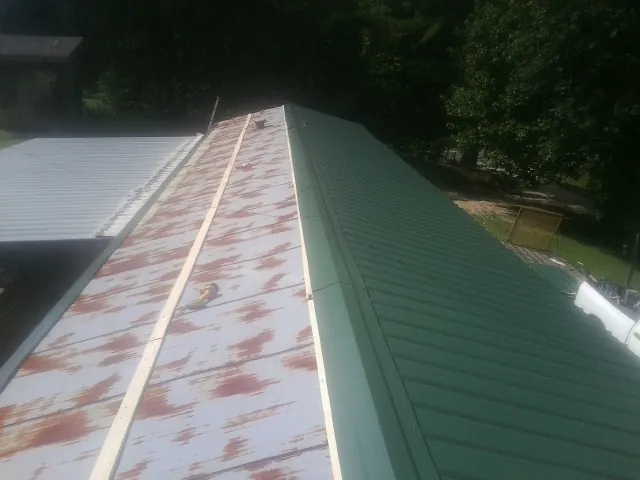 Old rusted panels beside newly installed green metal roofing — Wind Damage Roof Repair by Roofing Brothers in West New York