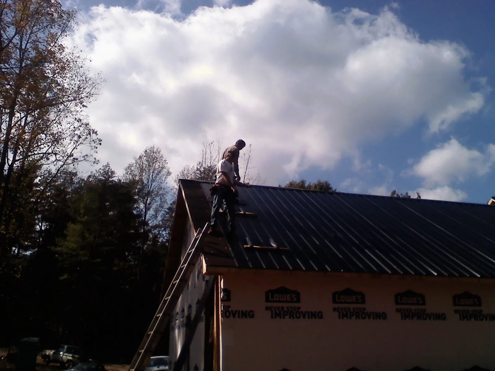 Roofer fastening dark metal panels high against a cloudy sky, from a Roof Inspection job in West New York
