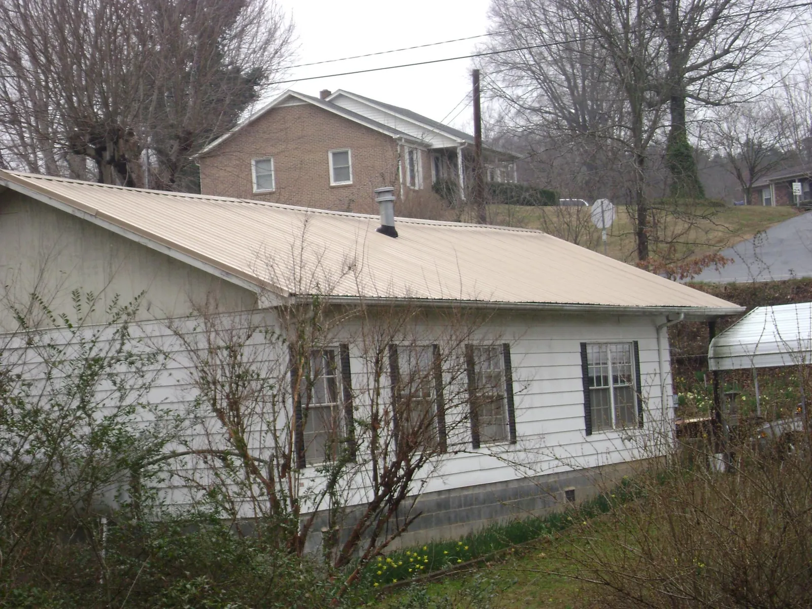 Tan metal roof on a white sided house set into a hillside — Commercial Roofing by Roofing Brothers in West New York